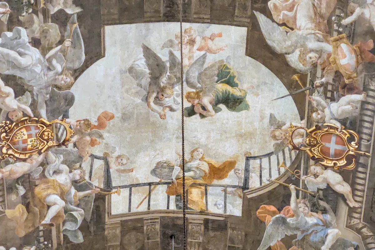 A painted ceiling in St John's Co-Cathedral, with angels, trumpets and gilt cartouches around a central oval scene
