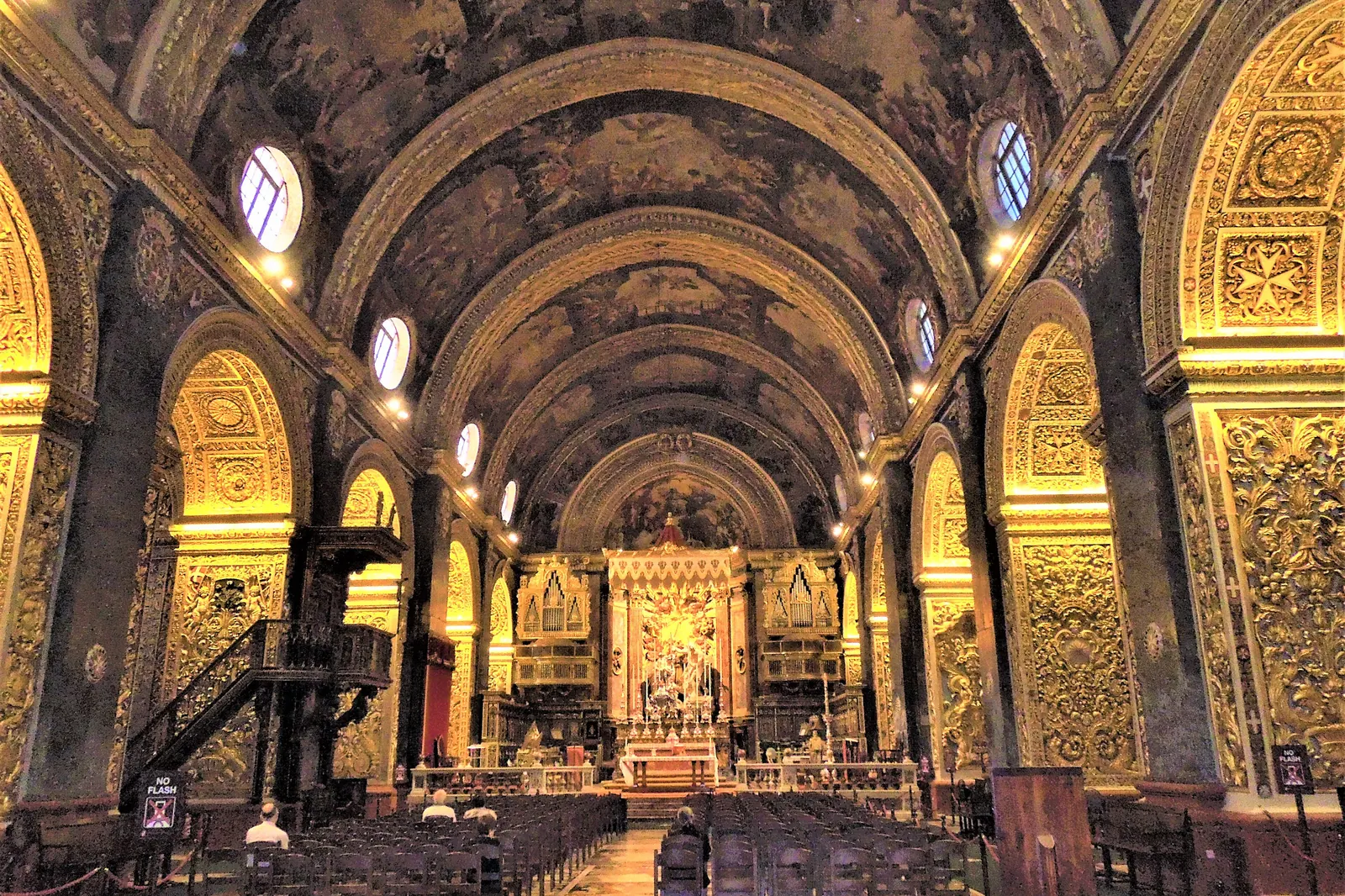 The nave of St John's Co-Cathedral looking towards the altar, under a painted barrel vault with walls covered in gilded carving